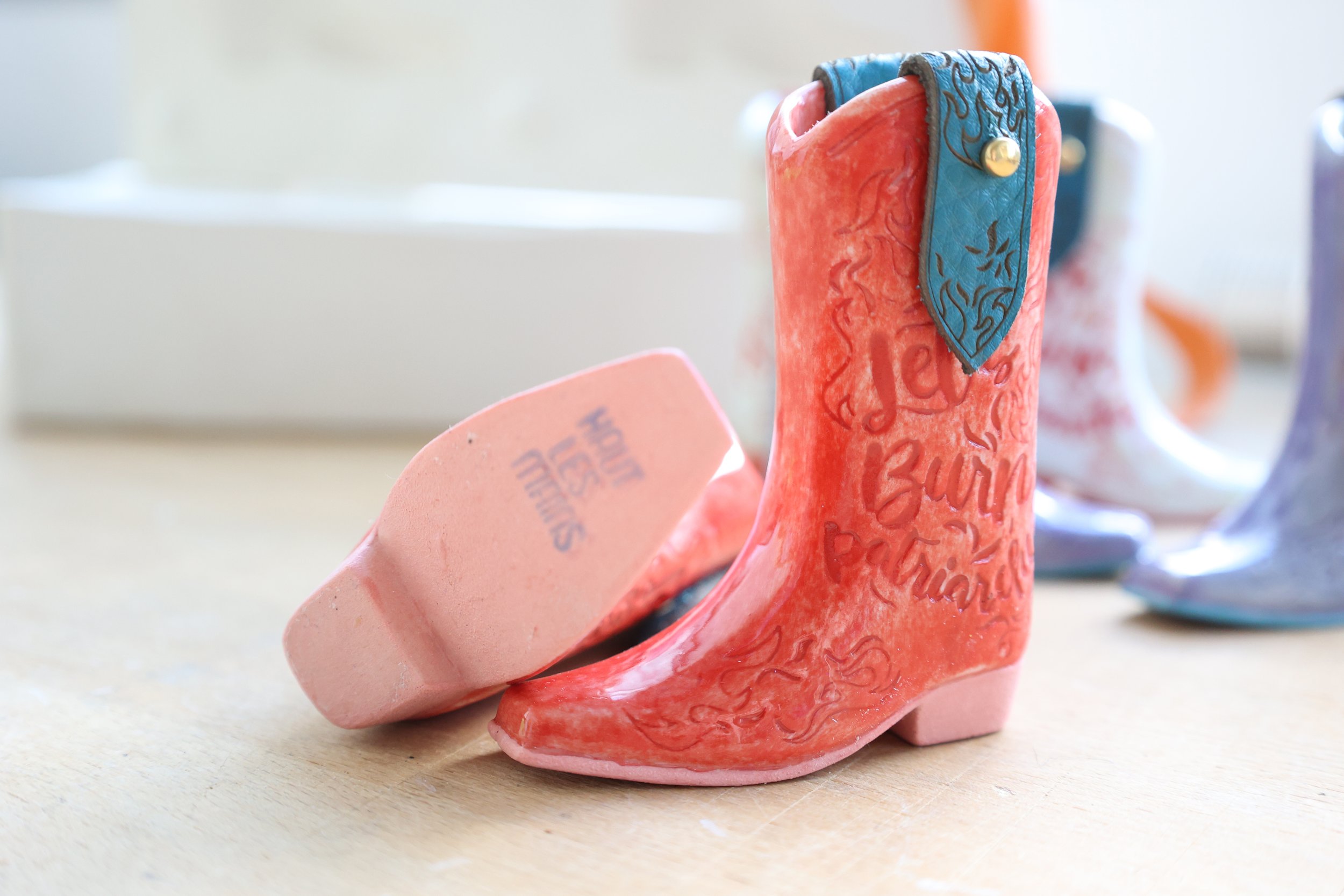 Bottes miniatures en céramique colorées sur une table, avec des motifs gravés et un texte 